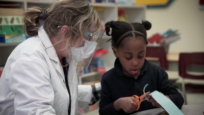 a girl cut a paper with the help of her teacher