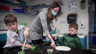 two students are painting in front of their teacher